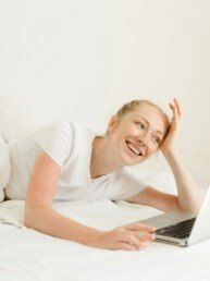 Smiling woman lying down with laptop in bed