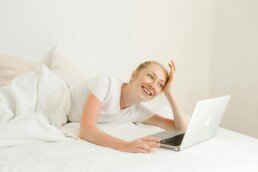 Smiling woman lying down with laptop in bed
