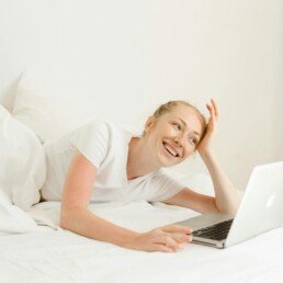 Smiling woman lying down with laptop in bed